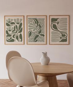 three paintings hang on the wall next to a table with two chairs and a vase