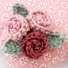 crocheted flowers are placed on top of a pink and green fabric pillow cover