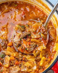 a ladle full of beef and cabbage soup in a red pot with a wooden spoon