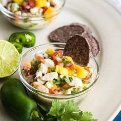 a white plate topped with two bowls filled with food next to limes and tortilla chips