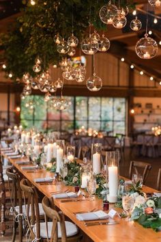 a long table with candles and greenery on it is surrounded by hanging glass globes