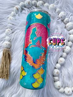 a blue and pink can with an image of a mermaid on it next to some white beads