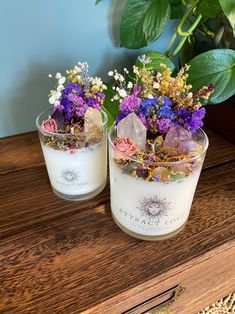 two candles with flowers in them sitting on a table next to a potted plant