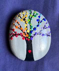 a painted rock with a tree on it and hearts in the leaves, sitting on a blue background