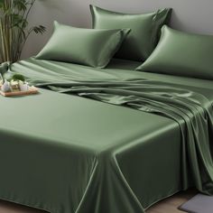 a bed covered in green sheets and pillows with a plant on the end of it