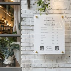 a white brick wall with a price list hanging on it's side and potted plants in the window