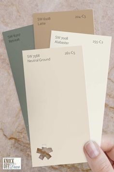 a hand is holding three different colors of paint swatches in front of a marble background