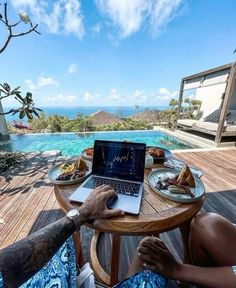 a man sitting at a table with a laptop on his lap in front of the pool