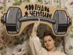 a woman holding up a wooden sign with a dumbbell on it