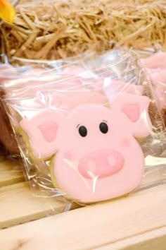 pink pig cookies sitting on top of a wooden table next to some hay and flowers