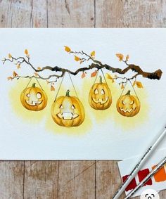 three jack o lantern pumpkins hanging from a tree branch with paintbrushes next to it