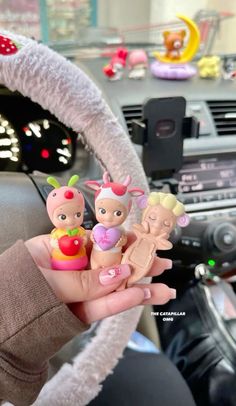 a person is holding some little dolls in their hand while driving a car with other toy figures on the steering wheel