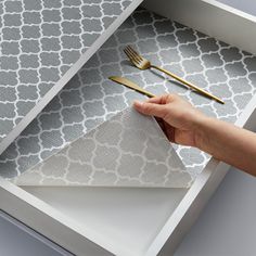 a person's hand reaching into a drawer with gold utensils