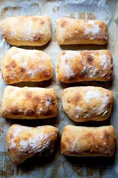 six loaves of bread sitting on top of a piece of wax paper covered in powdered sugar