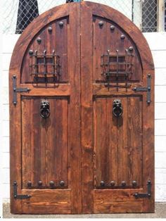 two large wooden doors with metal handles on each one and an arched window behind them