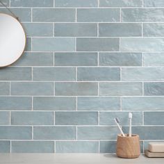 a mirror and toothbrush holder in front of a blue brick wall with a round mirror above it