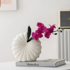 a white vase filled with pink flowers on top of a book