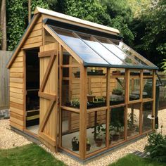 a small wooden greenhouse in the middle of a yard with lots of plants growing inside