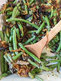 green beans and onions are mixed together in a white dish with a wooden spatula