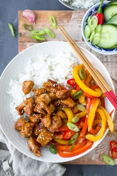 chicken and peppers with rice in a white bowl on a wooden table next to cucumbers