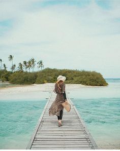 a woman walking across a wooden bridge near the ocean with an island in the background