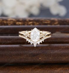 an engagement ring with a pear shaped diamond in the center on top of a wooden stand