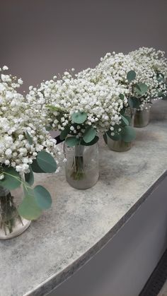 four vases filled with white flowers and greenery on top of a marble counter