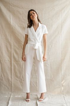 a woman standing in front of a white backdrop wearing a white top and wide legged pants