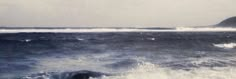 a person riding a surfboard on top of a wave in the ocean with an island in the background