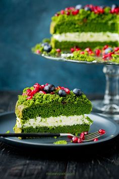 a piece of green cake on a plate with a fork next to it and another slice in the background