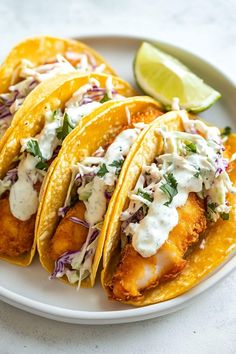 three fish tacos on a white plate with lime wedges