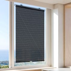 a room with a window covered in black and white polka dot pattern roller shades, overlooking the ocean