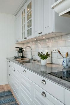 a kitchen with white cabinets and marble counter tops, along with a sink that has a potted plant on it