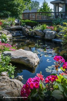 a pond with flowers and rocks in the foreground is surrounded by trees, bushes, and a house