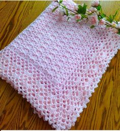 a pink crocheted blanket sitting on top of a wooden floor next to flowers