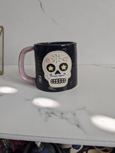 a black and pink coffee mug sitting on top of a white counter next to a clock