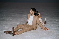 a man and woman are sitting on the ground in their wedding attire, posing for a photo