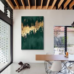 an abstract painting hangs on the wall above a dining room table with chairs and a dog laying on the floor