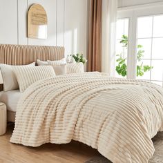 a bed with white comforter and pillows in a bedroom next to a large window