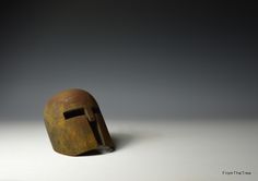 an old helmet is sitting on the floor in front of a gray background with no one around it