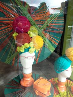 two mannequins with colorful hats and yarn on them in a store window