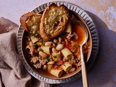 a bowl filled with pasta and beans on top of a table next to a spoon