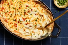 a casserole dish with cheese and vegetables on the side, next to a bowl of parsley