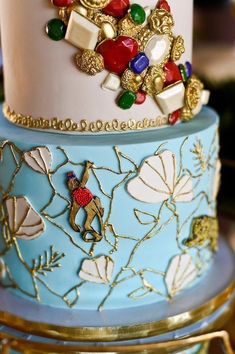 a three tiered cake with colorful decorations on it's sides and gold trimmings