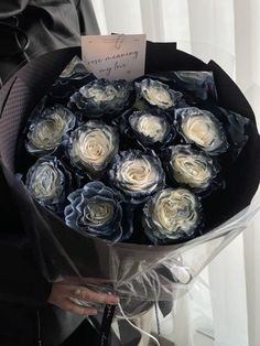 a woman holding a bouquet of white and grey roses with a note attached to it