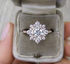 an engagement ring in a velvet box with the diamond center surrounded by smaller round brilliant cut diamonds