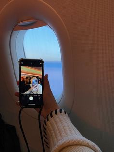 a person holding up a cell phone to take a photo on an airplane window sill