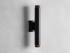 a wall mounted light on the side of a white wall next to a black pole