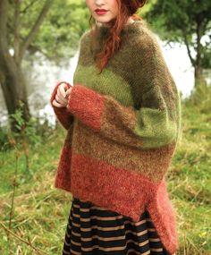 a woman standing in the grass wearing a colorful sweater and hat with her hands on her hips