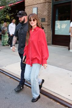 a woman in red shirt and jeans walking on sidewalk next to man wearing black hat